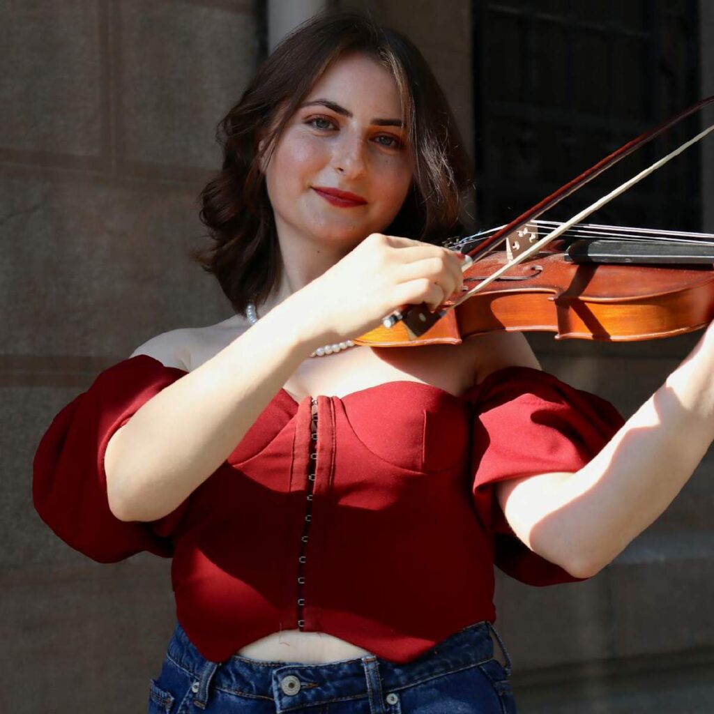 Picture of a music teacher posing for music teacher jobs. This teacher is smiling while holding her violin.